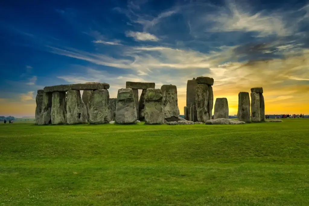 Sunset over the historic Stonehenge in England highlighting the mystical stone circle with colorful sky and lush green field.