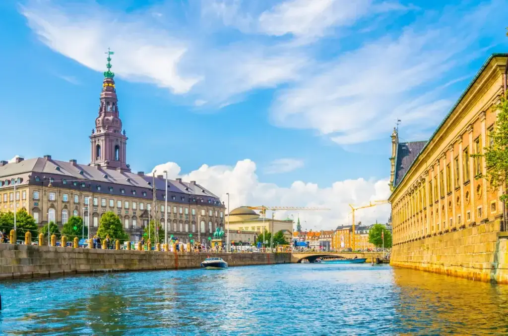 View of Christiansborg Slot Palace along the canal in Copenhagen, Denmark, showcasing the historic architecture and vibrant urban life.