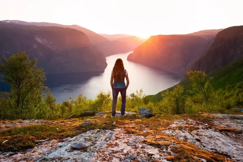 Woman enjoying a breathtaking sunset over Aurlandsfjord in Norway, showcasing the serene beauty of Scandinavian fjords.