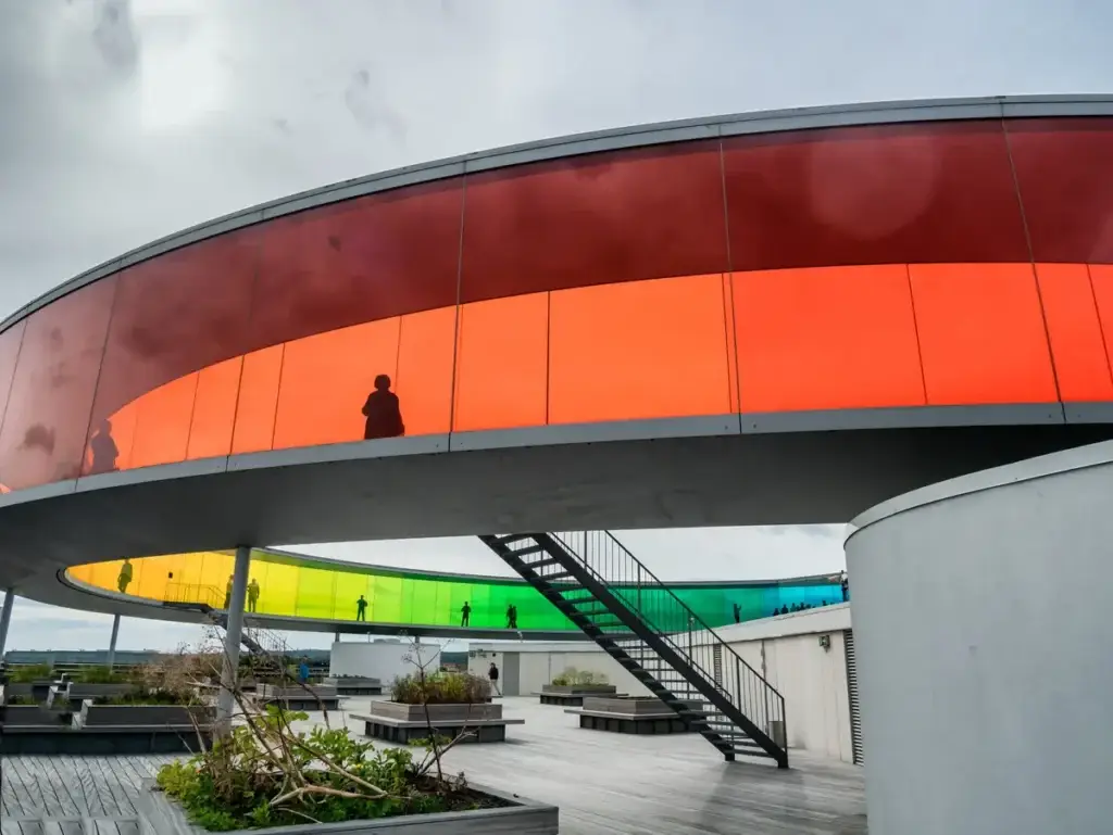 Visitors explore the colorful, circular rooftop walkway of the Aros Art Museum in Aarhus, Denmark, showcasing modern architecture and urban design.