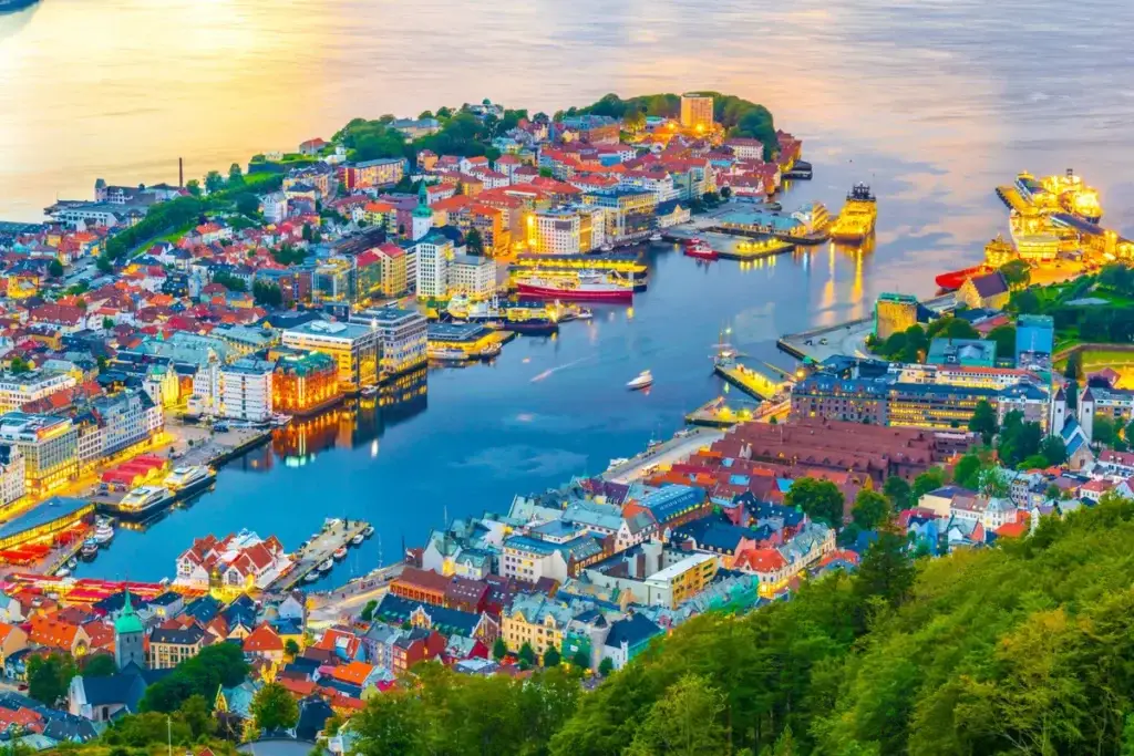 Panoramic sunset view of Bergen harbor and cityscape seen from Mount Floyen, showcasing historical buildings and bustling docks in Norway.