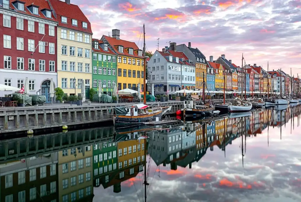 Sunrise over Nyhavn Canal in Copenhagen with colorful houses reflected in calm waters and docked boats.