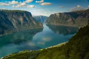 Panoramic view of Aurlandsfjord from Stegastein viewpoint, showcasing the serene waters and dramatic green cliffs under a bright sky, in Vestland, Norway.
