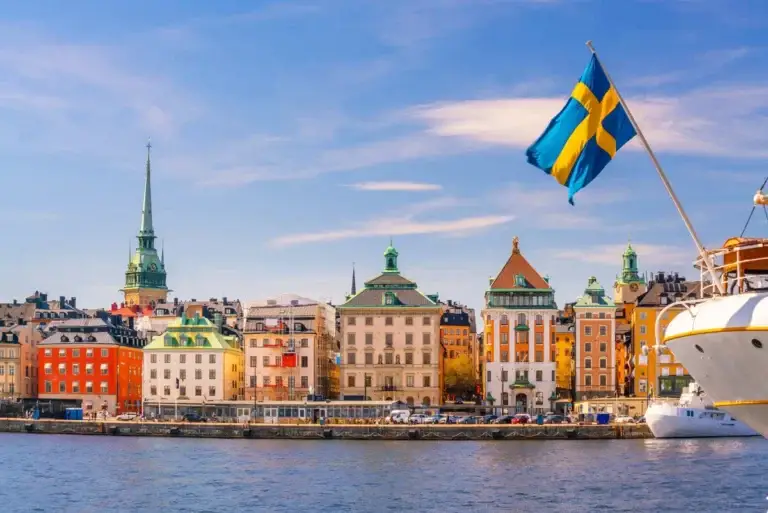 Scenic view of Stockholm's old town with vibrant buildings and the Swedish flag waving from a boat, highlighting the cityscape of Sweden.