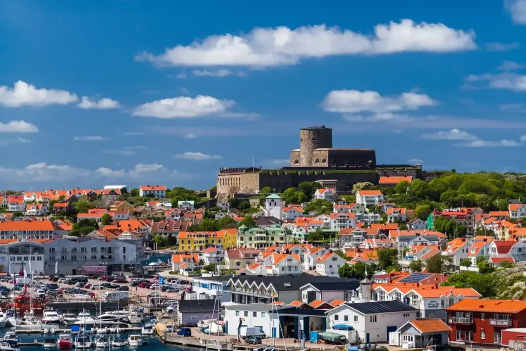 Panoramic view of Marstrand in Bohuslan, Sweden, showcasing the historic Carlsten Fortress atop the island surrounded by colorful houses and busy marina.