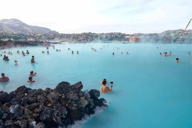 Tourists enjoying a relaxing soak in the geothermal waters of Blue Lagoon, Iceland, surrounded by rugged lava rocks.