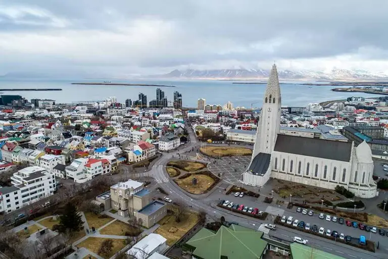 Aerial view of Reykjavik, Iceland showcasing the Hallgrimskirkja church and scenic surroundings with colorful rooftops and the ocean in the background.