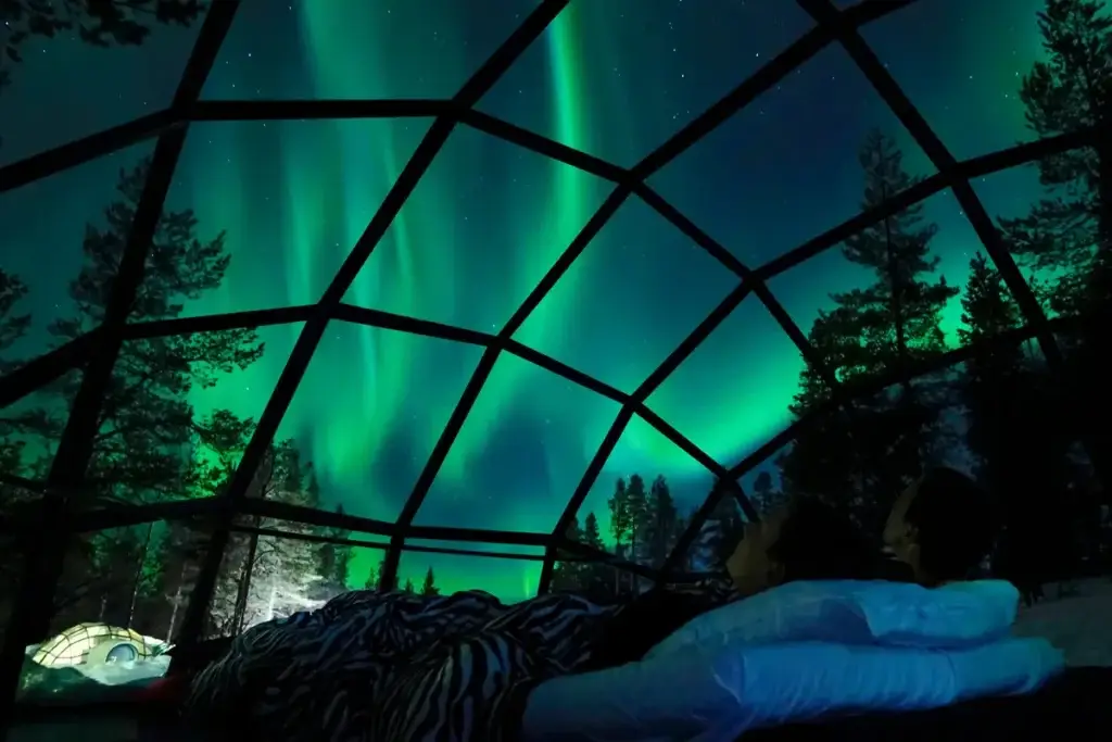 Young Caucasian couple enjoying a view of the Northern Lights from inside a glass igloo in the Scandinavian wilderness, perfect for romantic getaways and unique travel experiences.