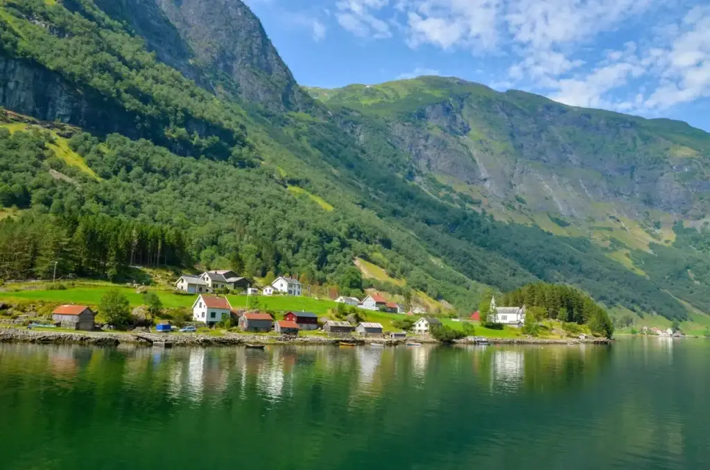 Scenic view of Sognefjord with the picturesque village of Bakka near Gudvangen in Norway, showcasing traditional houses and lush green landscapes by the water.