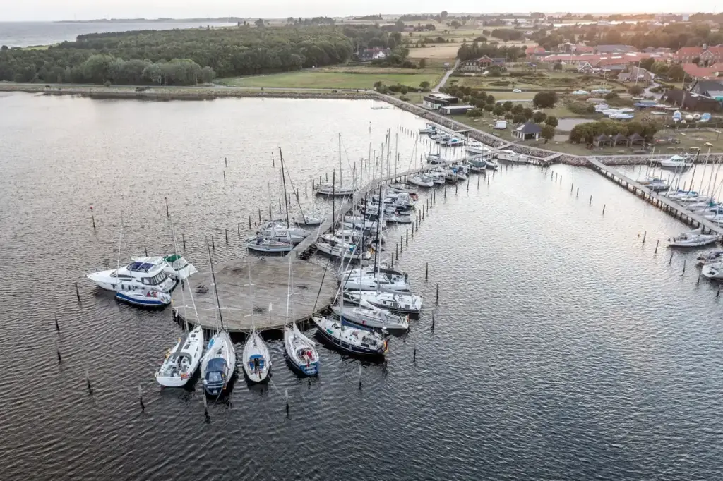 Aerial view of Marstal harbor in Scandinavia during sunset, showcasing numerous moored yachts and the serene coastal landscape.