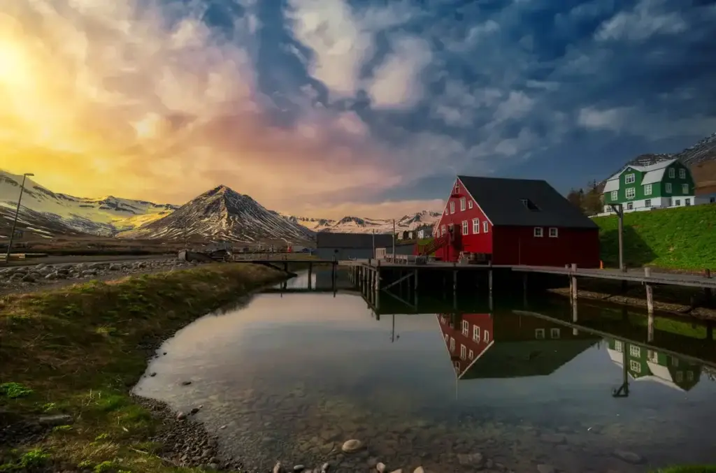 Picturesque view of Siglufjordur, a charming fishing village in North Iceland, with colorful houses reflecting in calm waters against a backdrop of snow-capped mountains.