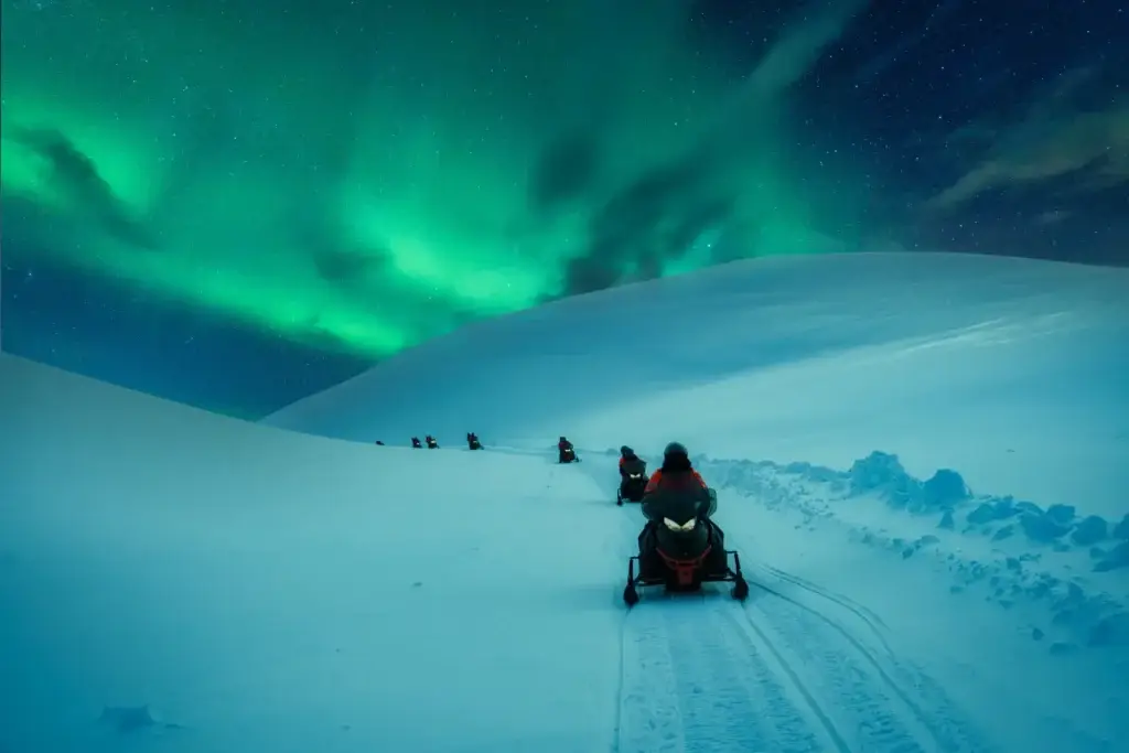 Tourists on a snowmobile adventure across snowy mountain under the aurora borealis in Scandinavia during winter.