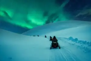 Tourists on a snowmobile adventure across snowy mountain under the aurora borealis in Scandinavia during winter.