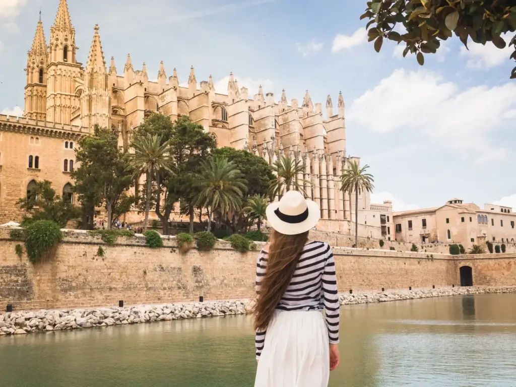 Stylish woman in a straw hat overlooking the Cathedral of Santa Maria and historic buildings along the river in Palma de Mallorca, Spain