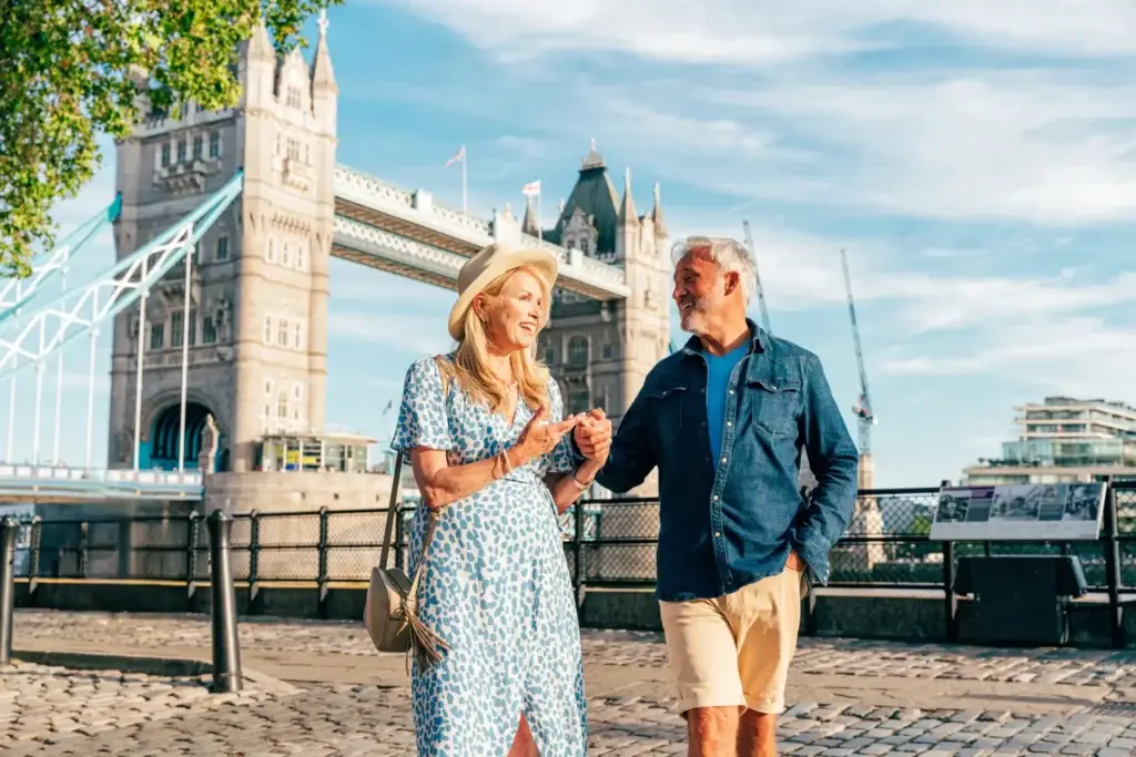 Happy senior couple enjoying a sunny day at Tower Bridge in London, showcasing a joyful moment of tourism in the city.