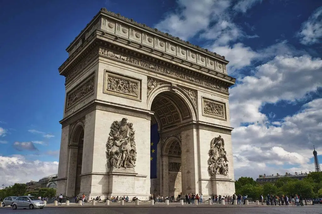 Arc de Triomphe in Paris, France on a sunny day showing intricate sculptures and tourists enjoying the landmark.