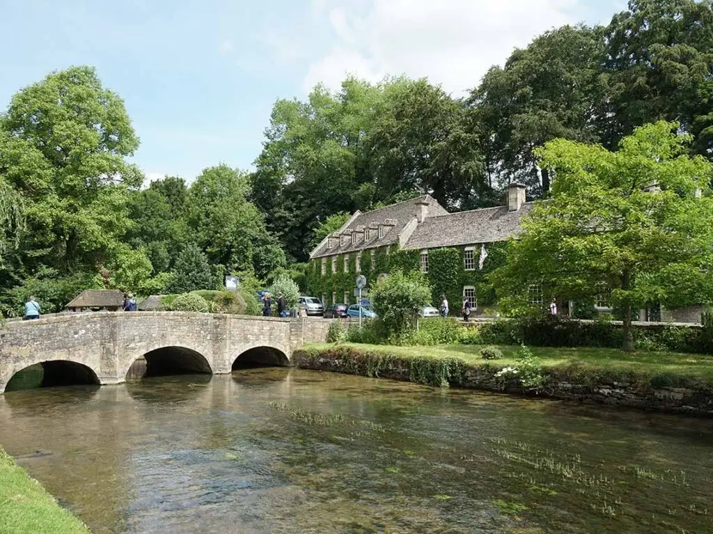 Scenic view of a serene river and an ancient stone bridge in the Cotswolds, England, featuring lush greenery and traditional architecture, ideal for tourists exploring rural UK.