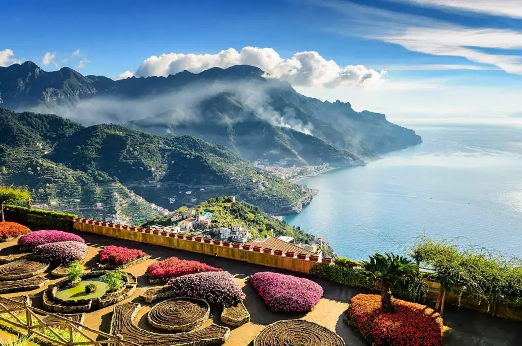 Breathtaking view of Ravello, Italy, showcasing vibrant floral gardens and the expansive Amalfi coast under a clear blue sky.