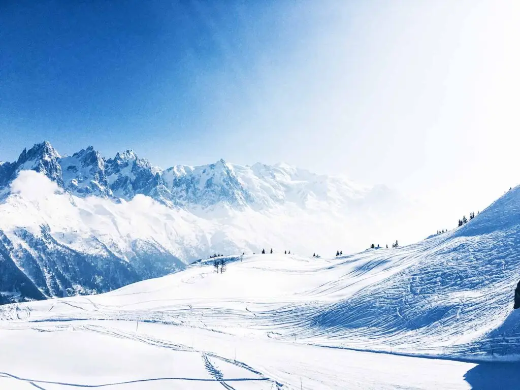 Panoramic view of snow-covered French Alps in Chamonix, France, showing ski slopes and majestic mountain peaks under a bright blue sky.