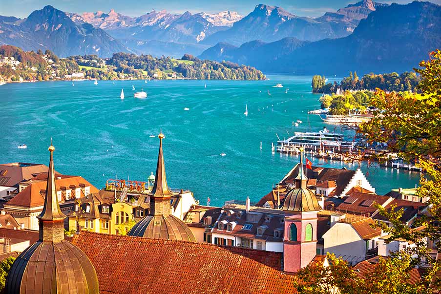 Panoramic view of Lake Lucerne in Switzerland showing vibrant cityscape, historic architecture, and alpine mountains in the background.