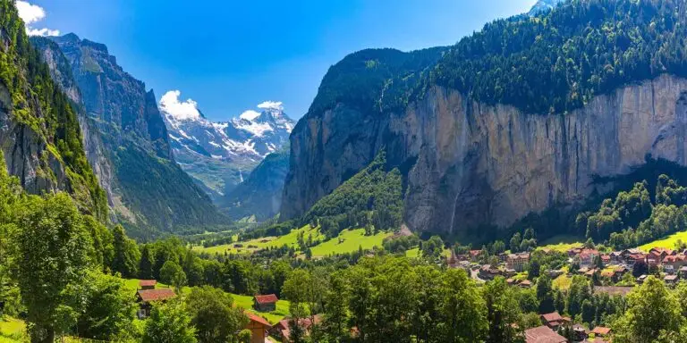 Breathtaking view of Lauterbrunnen Valley in Switzerland, showcasing steep cliffs, a quaint village, lush greenery, and distant snow-capped mountains.
