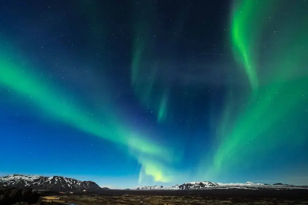 Spectacular view of the Northern Lights over the Blue Lagoon in Iceland at night with starry sky and snow-capped mountains in the background