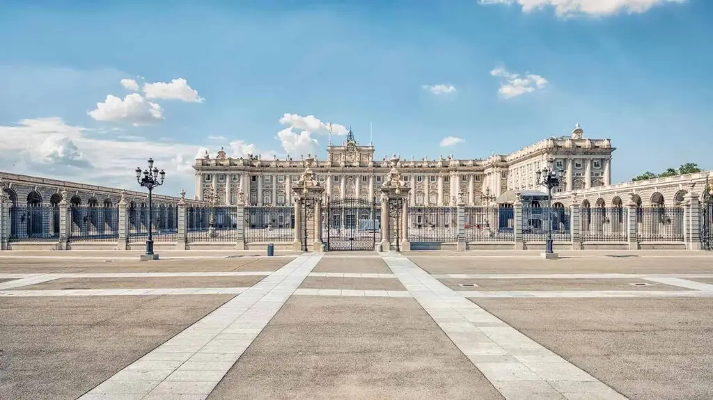 Panoramic view of the Royal Palace of Madrid, Spain, showcasing its majestic facade and ornate gates under a clear blue sky.