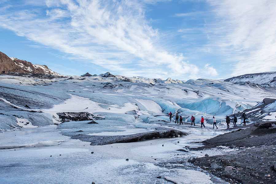 Tourists walking on the icy surface of Sólheimajökull Glacier in Iceland, showcasing the glacier's dramatic ice formations under a clear blue sky.