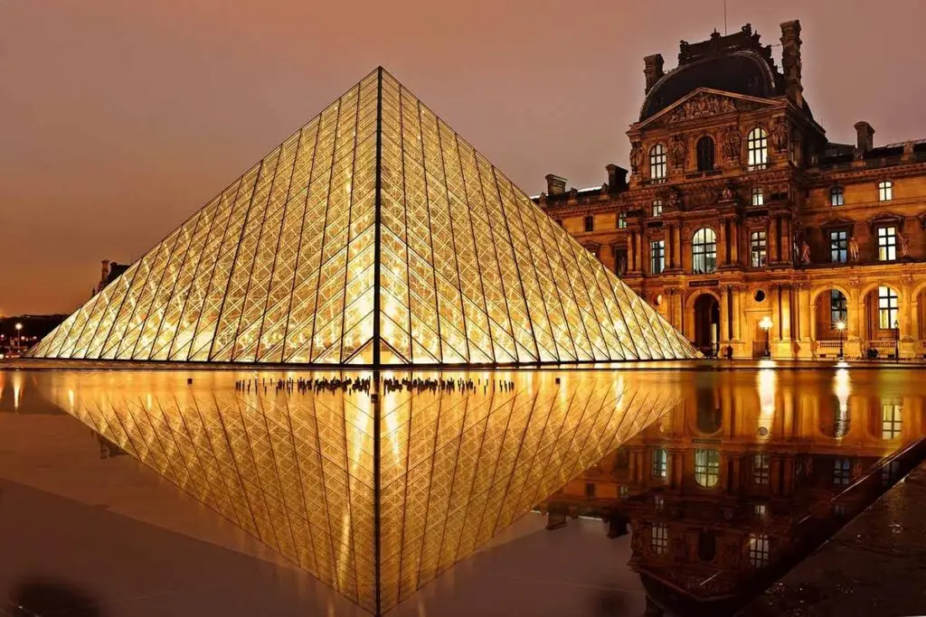 Illuminated Louvre Pyramid at dusk with reflection on water surface, a major landmark in Paris, France