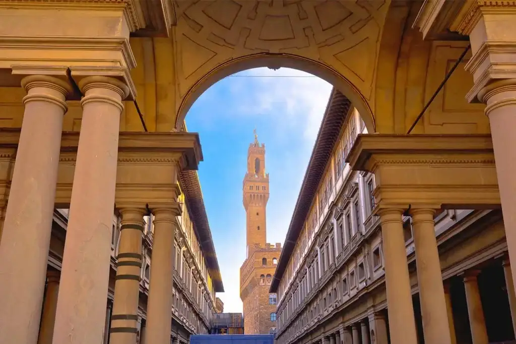 View of the iconic Palazzo Vecchio tower seen through an archway of the Uffizi Gallery in Florence, Italy, showcasing Renaissance architecture and the rich history of the region.