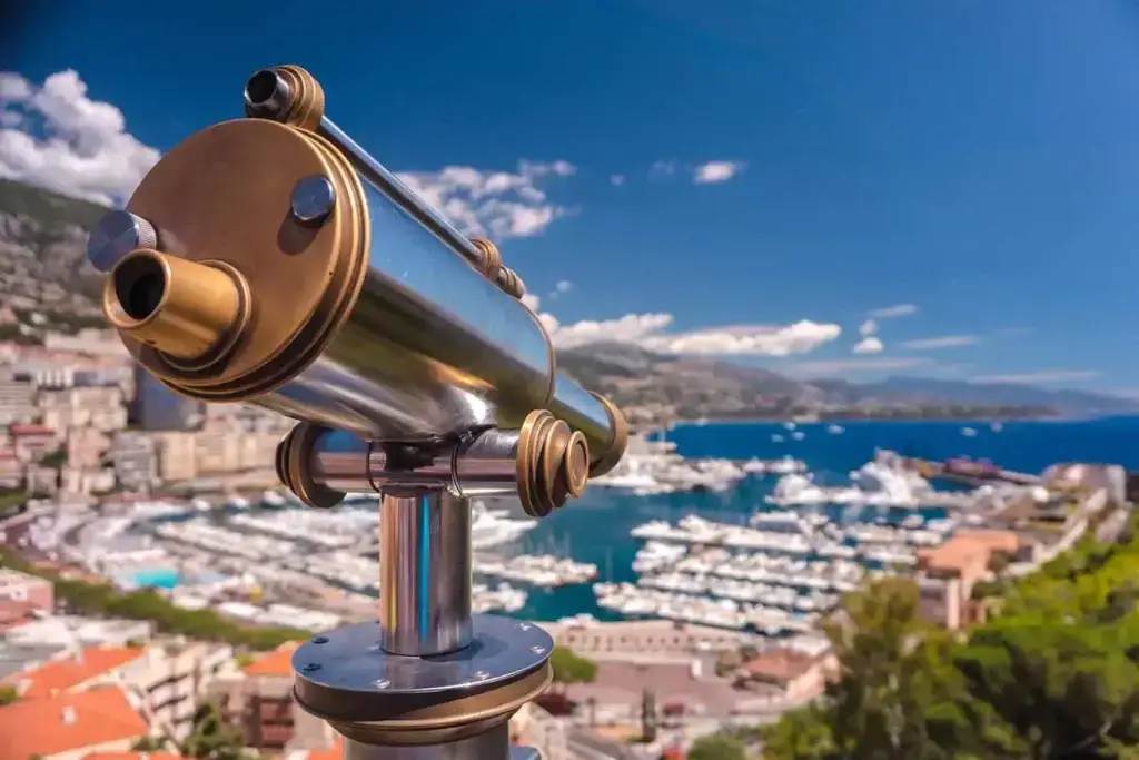 Telescope viewing point overlooking the scenic Monaco marina filled with yachts under a clear blue sky.