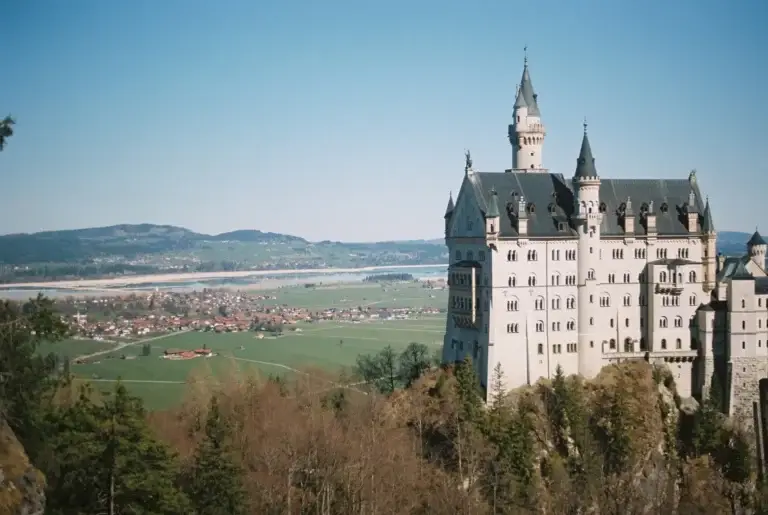 Neuschwanstein Castle in Germany, showcasing its fairy-tale architecture with intricate towers, nestled on a forested hill overlooking a scenic landscape.