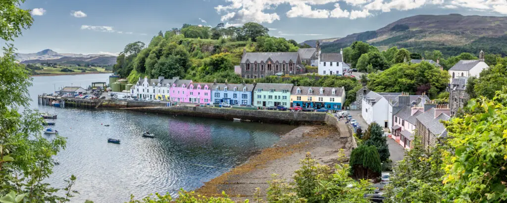 Colorful waterfront houses along Portree Harbour on the Isle of Skye, Scotland, with scenic hills, boats, and a charming village view popular for European travel and photography tours