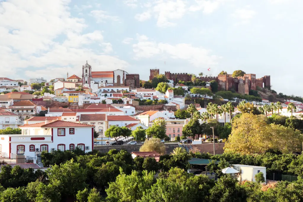 View of Silves town and the historic Silves Castle in the Algarve region of Portugal, surrounded by traditional whitewashed houses and lush greenery