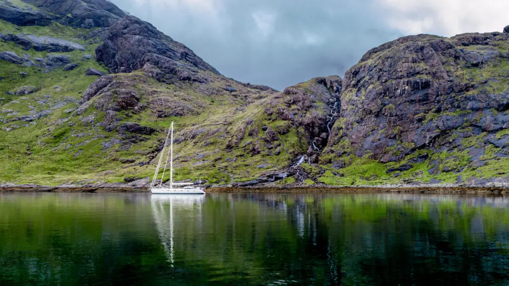 Sailboat anchored on the calm waters of Loch Coruisk surrounded by rugged green mountains on the Isle of Skye, Scotland