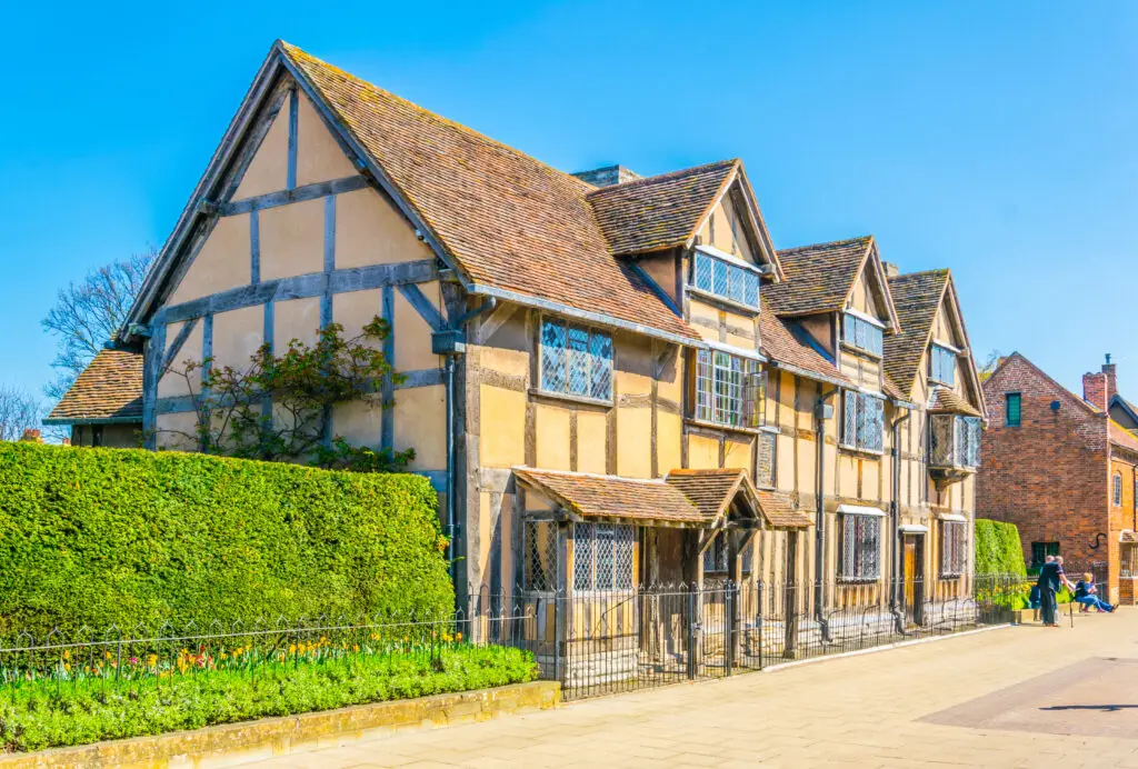 Tourists walking beside William Shakespeare’s birthplace in Stratford-upon-Avon, England, featuring traditional Tudor architecture and a popular historic attraction.