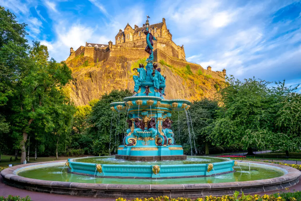 Edinburgh Castle and Ross Fountain in Princes Street Gardens, Scotland, surrounded by lush greenery and blue sky, a famous historic landmark and tourist attraction in Edinburgh