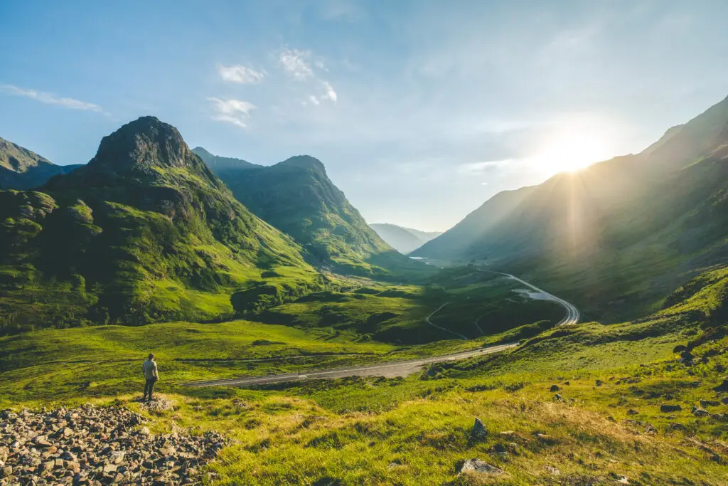 Man standing on a hillside overlooking the sunrise across Glencoe valley in the Scottish Highlands, Scotland, during a scenic Europe private tour