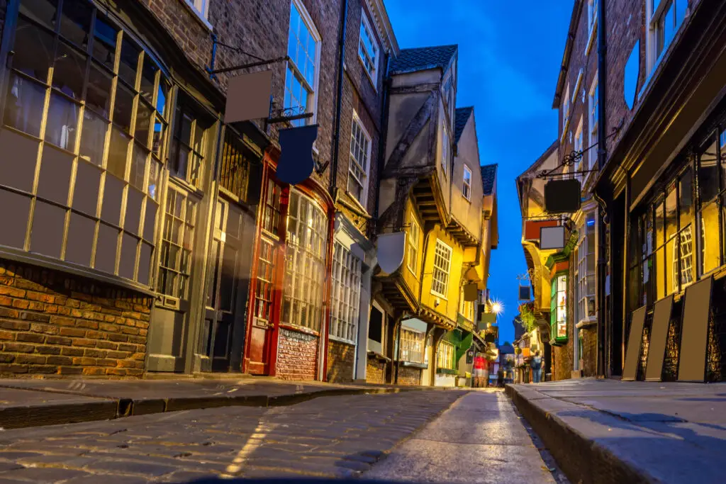 Historic York Shambles street at sunset with illuminated medieval timber-framed buildings and cobblestone path in York, England