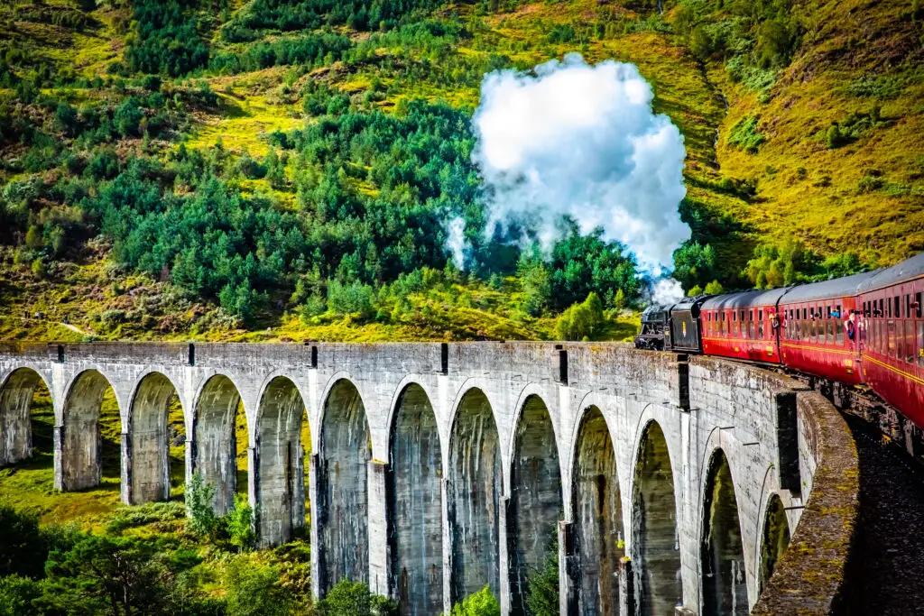 Steam train crossing the Glenfinnan Railway Viaduct in the Scottish Highlands, Scotland, surrounded by lush green hills and scenic landscape