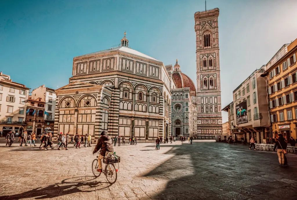Tourists walking and cycling in Piazza del Duomo, featuring Florence Cathedral, Giotto’s Bell Tower, and the Baptistery, a famous landmark in Florence, Italy