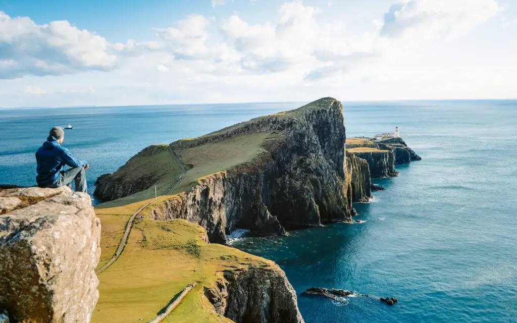 Tourist admiring the scenic cliffs and lighthouse at Neist Point on the Isle of Skye, Scotland, a popular travel destination for European private tours and nature photography.