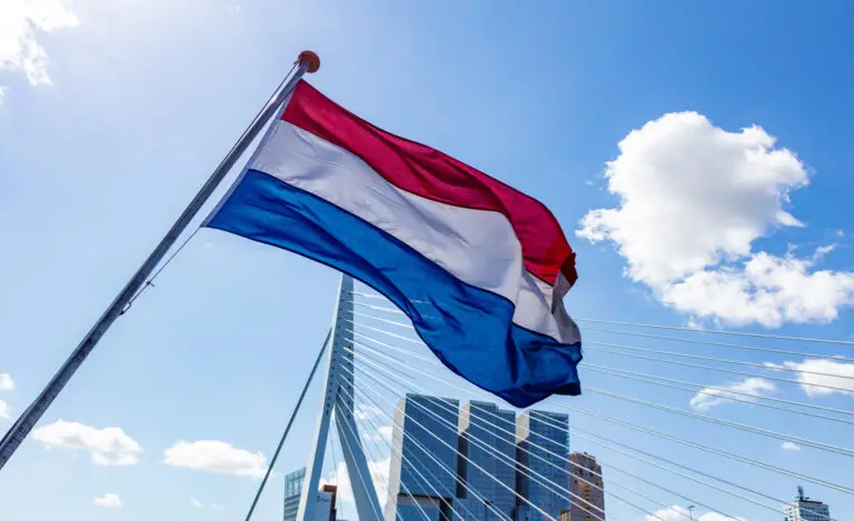 Dutch flag waving in front of the Erasmus Bridge and modern city skyline in Rotterdam, Netherlands on a sunny day