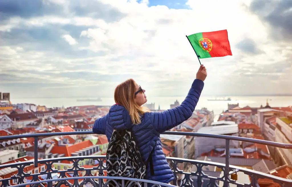 Tourist holding Portuguese flag overlooking Lisbon city rooftops and Tagus River, Portugal sightseeing viewpoint