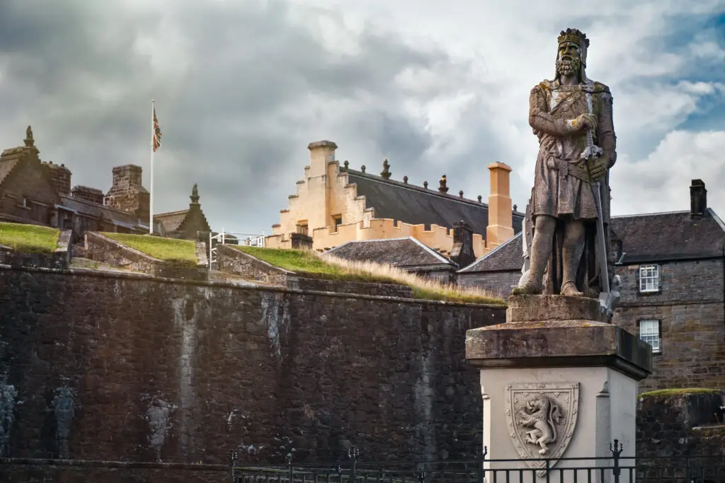 Statue of a Scottish king outside Stirling Castle in Scotland with historic stone walls and buildings under a cloudy sky