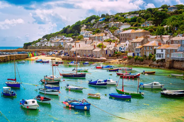 Colorful fishing boats in the scenic harbor of Mousehole village, Cornwall, England, surrounded by stone cottages and coastal hills, a popular travel destination in southwest England.