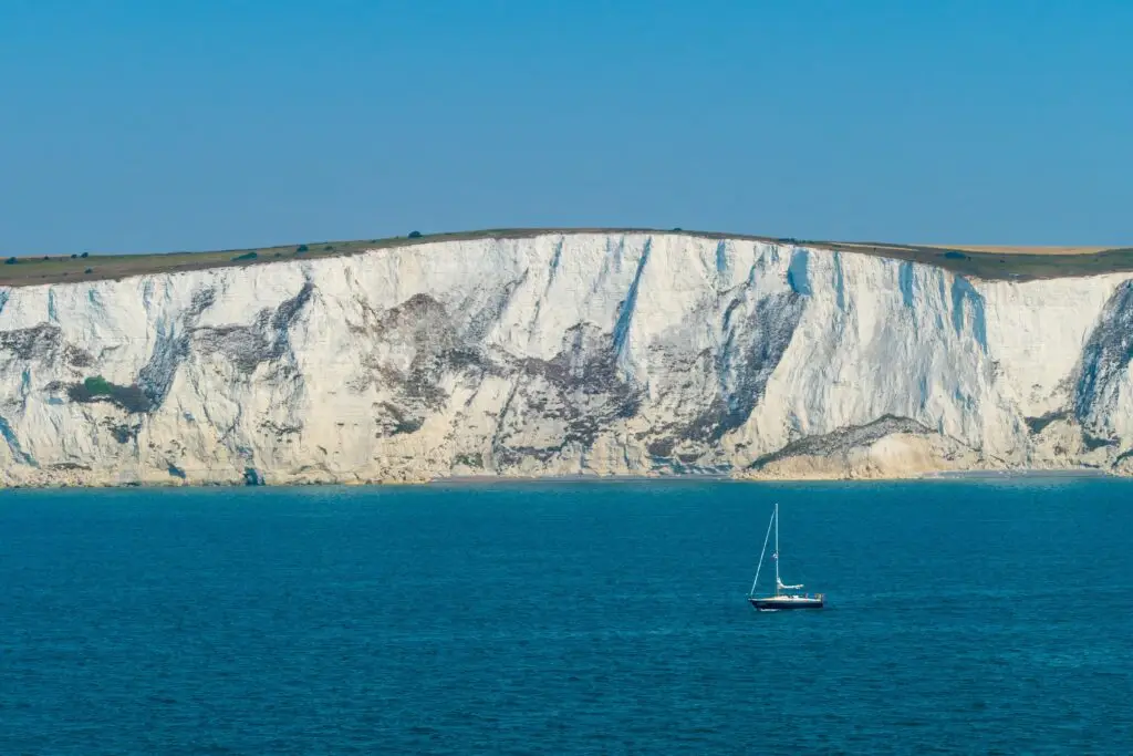 Sailboat on the blue waters below the White Cliffs of Dover in England, a famous coastal landmark and popular tourist attraction.