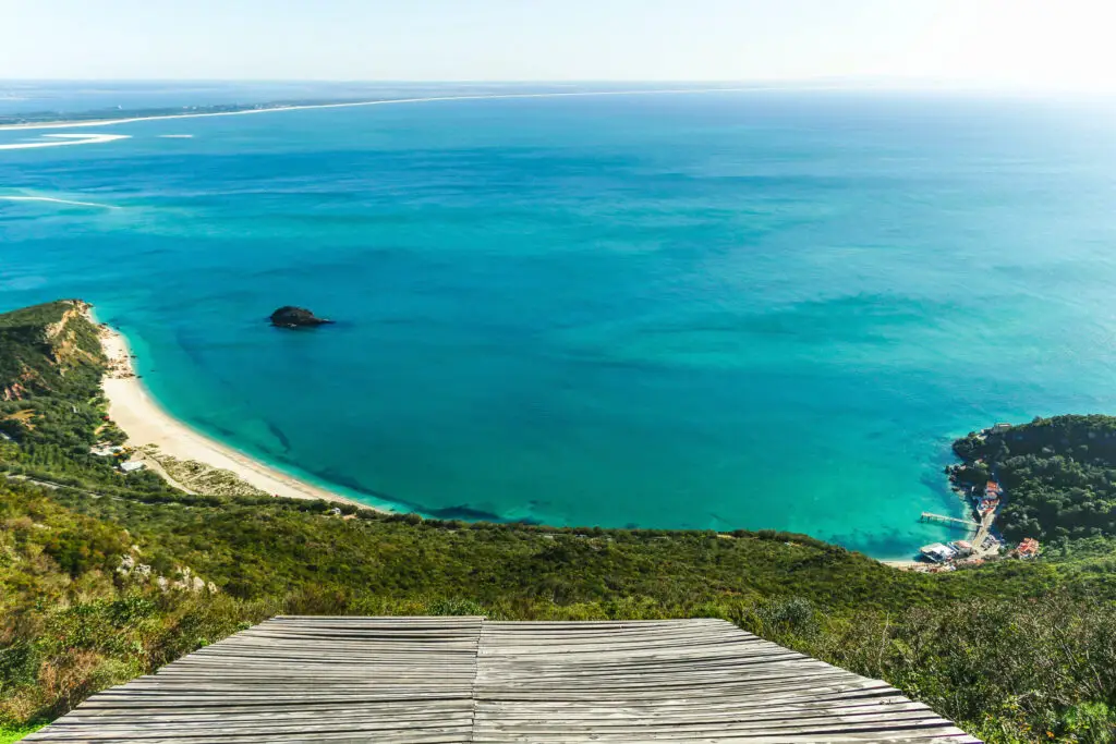 Scenic view of the turquoise coastline and beaches of Serra da Arrábida National Park in Portugal with lush green hills and clear blue Atlantic Ocean waters