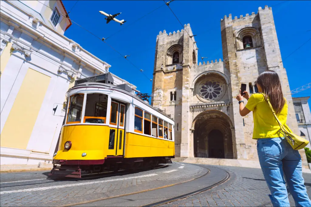 Yellow tram passing by Lisbon Cathedral with a tourist taking photos in Lisbon, Portugal