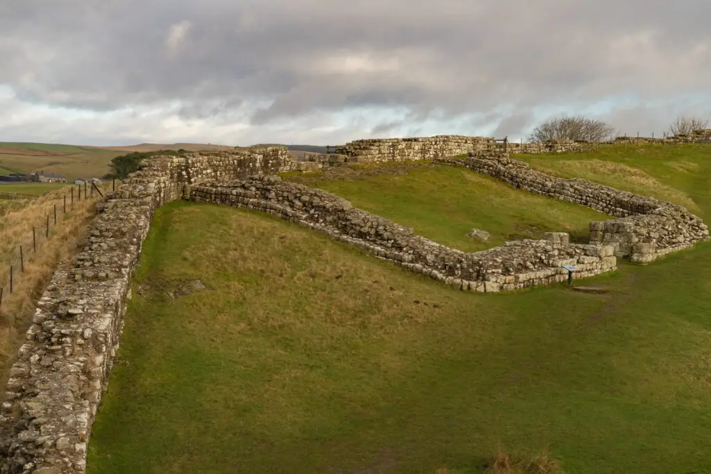 Ancient stone ruins of Milecastle 42 on Hadrian’s Wall in Northumberland, England, surrounded by green hills and countryside under a cloudy sky